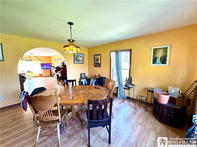dining area featuring arched walkways, baseboards, and wood finished floors