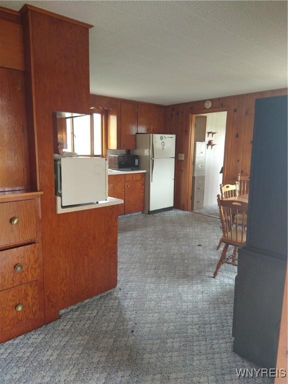 kitchen with brown cabinets, light countertops, wood walls, carpet, and freestanding refrigerator