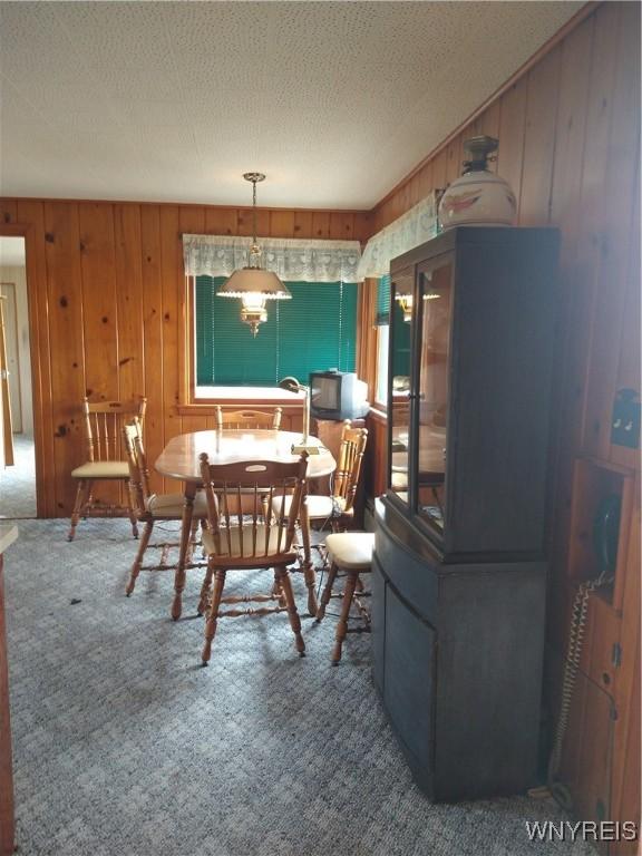 carpeted dining space with wood walls and a textured ceiling