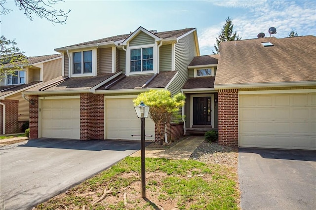 view of property featuring brick siding, a shingled roof, an attached garage, and aphalt driveway