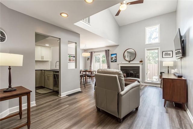 living area with a ceiling fan, baseboards, a glass covered fireplace, and dark wood-type flooring
