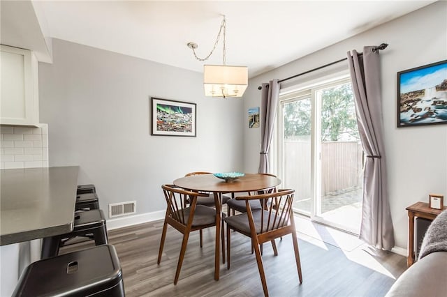dining space with a notable chandelier, baseboards, visible vents, and wood finished floors