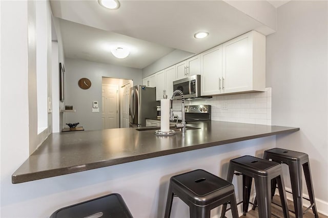 kitchen featuring dark countertops, appliances with stainless steel finishes, a sink, white cabinetry, and tasteful backsplash