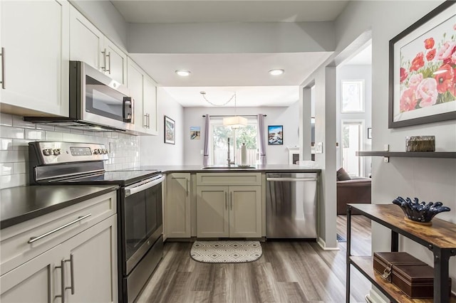 kitchen featuring dark wood-style flooring, a peninsula, dark countertops, a sink, and appliances with stainless steel finishes