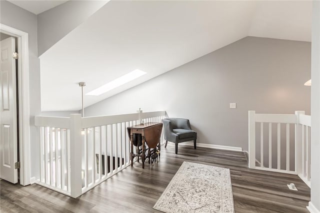 interior space with vaulted ceiling with skylight, baseboards, wood finished floors, and an upstairs landing