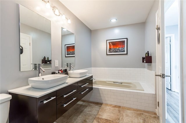 bathroom featuring double vanity, a sink, a bath, and toilet