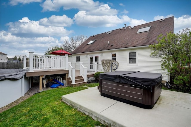 rear view of property with a wooden deck, roof with shingles, a patio area, a hot tub, and a yard