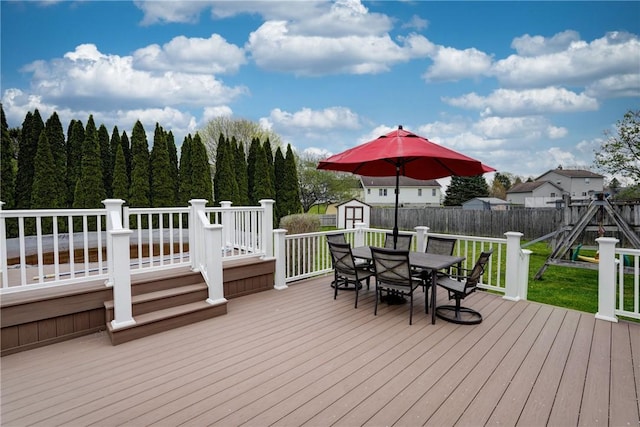 wooden deck featuring outdoor dining area, an outdoor structure, a shed, a fenced backyard, and a yard