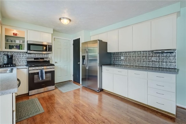 kitchen featuring white cabinets, backsplash, stainless steel appliances, and light wood-style flooring