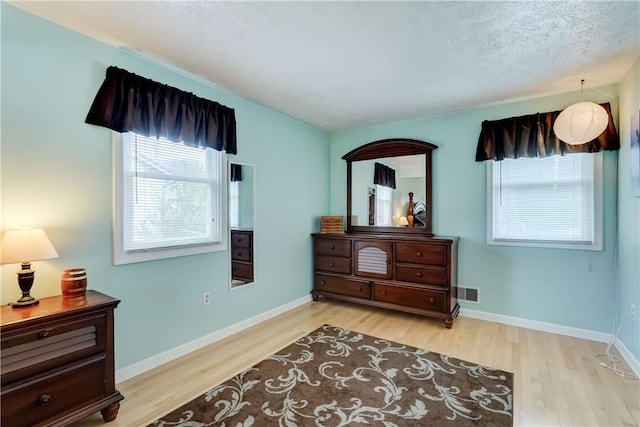 bedroom featuring baseboards, wood finished floors, visible vents, and multiple windows