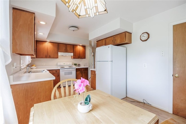 kitchen with white appliances, under cabinet range hood, brown cabinetry, and a sink