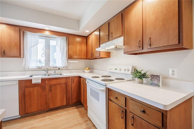 kitchen with white appliances, light countertops, under cabinet range hood, brown cabinets, and a sink