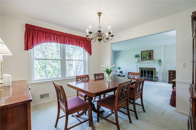 dining room featuring a chandelier, light carpet, visible vents, and a glass covered fireplace