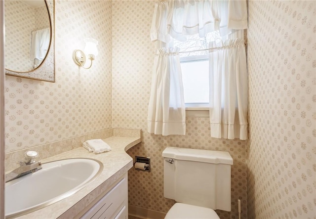 bathroom with vanity, toilet, and wallpapered walls