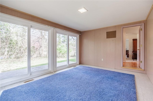 carpeted spare room with wooden walls and visible vents