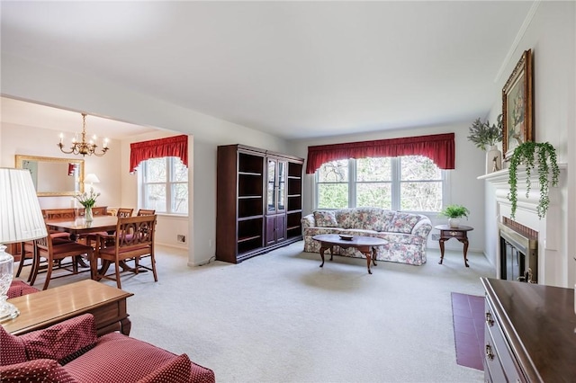 living room featuring an inviting chandelier, baseboards, a glass covered fireplace, and light carpet