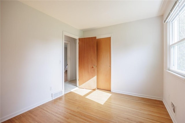 unfurnished bedroom with visible vents, light wood-style flooring, baseboards, and a closet