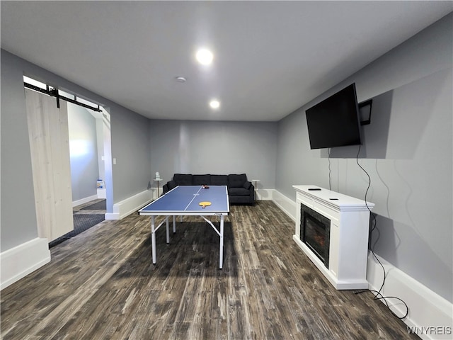 game room with a glass covered fireplace, baseboards, a barn door, and wood finished floors