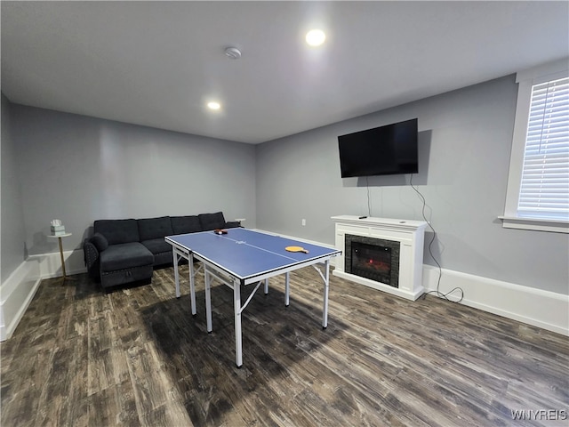 rec room featuring baseboards, a warm lit fireplace, dark wood-style floors, and recessed lighting