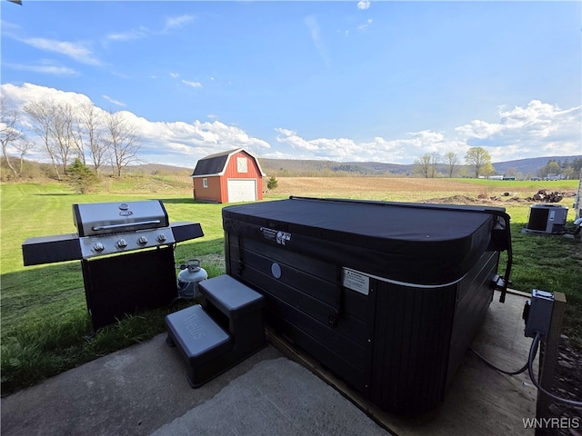 view of patio with a grill, a rural view, a barn, a hot tub, and an outbuilding
