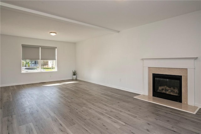 unfurnished living room with baseboards, a glass covered fireplace, wood finished floors, and beamed ceiling