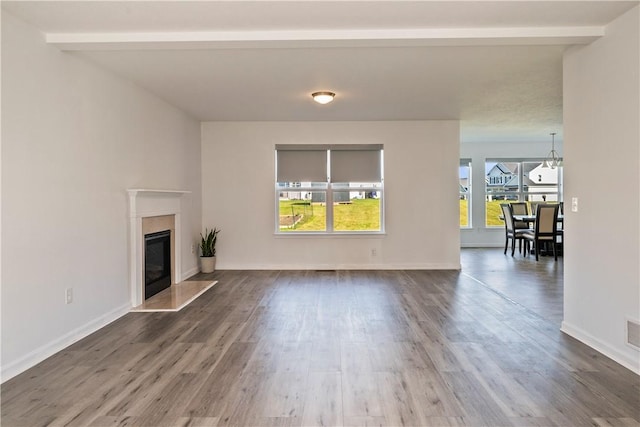 unfurnished living room with a high end fireplace, baseboards, beamed ceiling, and wood finished floors