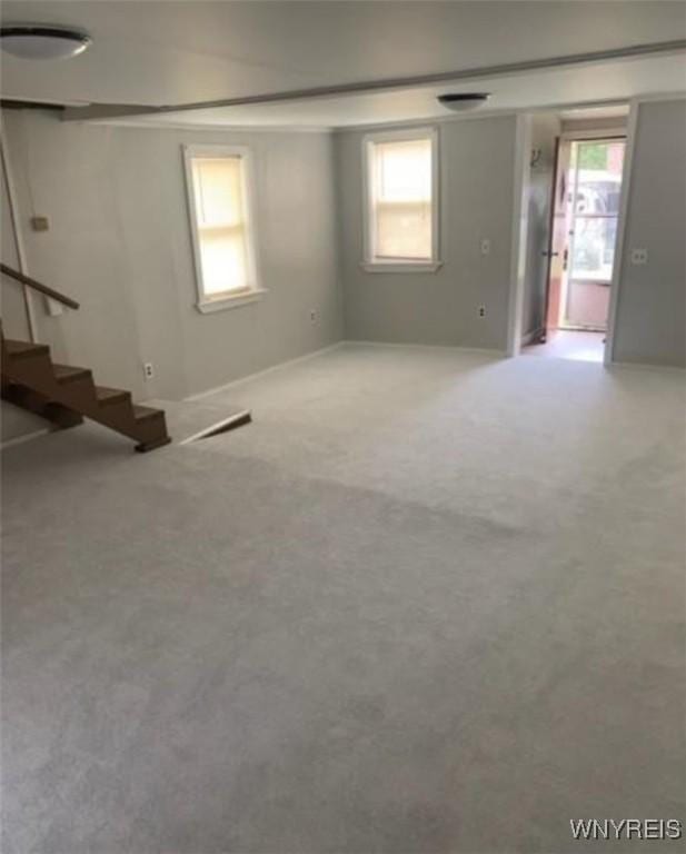 unfurnished living room with baseboards, carpet flooring, stairs, and a wealth of natural light