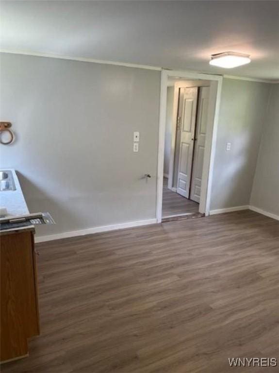 spare room featuring dark wood-type flooring, ornamental molding, and baseboards
