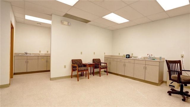 interior space featuring baseboards, a sink, a paneled ceiling, and light floors
