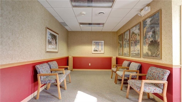 living area with carpet floors, a paneled ceiling, and wallpapered walls