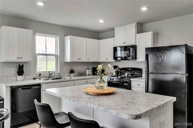 kitchen with a kitchen breakfast bar, light countertops, white cabinetry, a sink, and black appliances