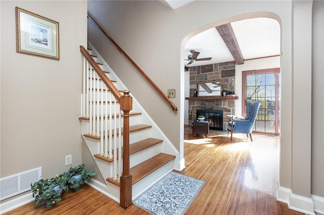 stairway with a ceiling fan, visible vents, arched walkways, wood finished floors, and baseboards