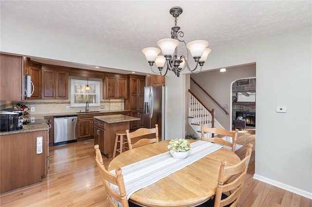 dining area with light wood-style floors, a stone fireplace, stairway, a textured ceiling, and a notable chandelier