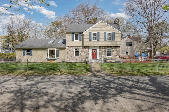 colonial inspired home with a fenced front yard, a front yard, a chimney, and stone siding