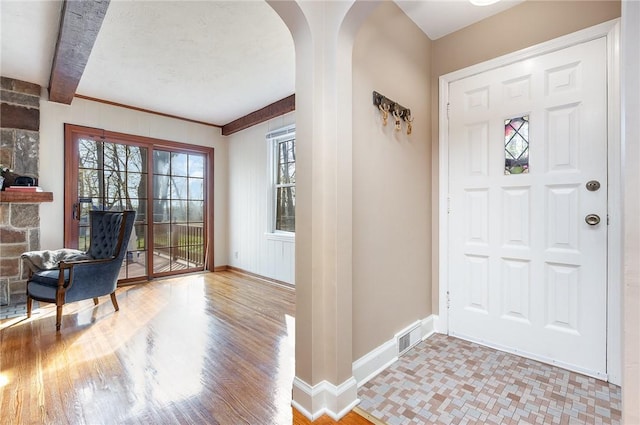 entryway with visible vents, beamed ceiling, baseboards, arched walkways, and light wood finished floors