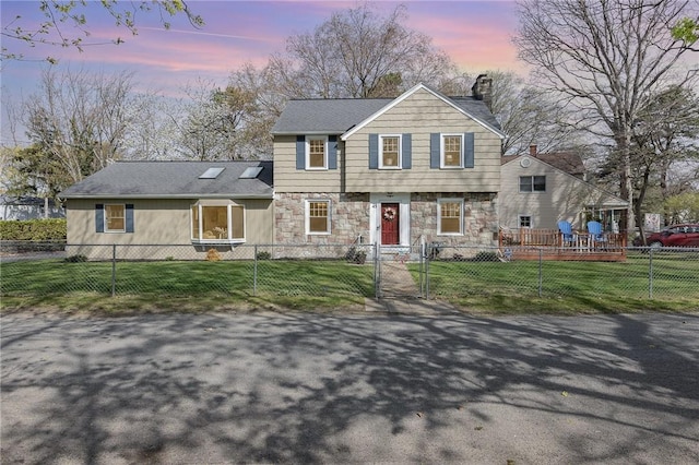 colonial home featuring a fenced front yard, a front yard, a chimney, and stone siding