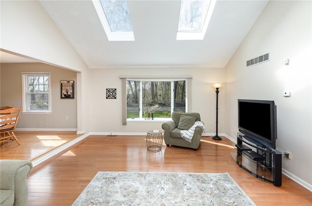 living area with a skylight, high vaulted ceiling, light wood-style flooring, and visible vents