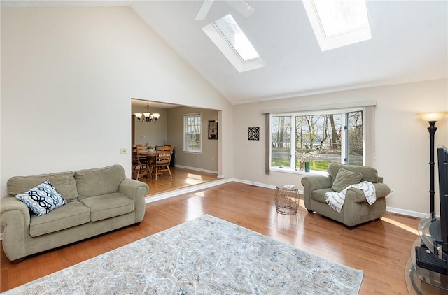 living area with high vaulted ceiling, a chandelier, a skylight, and wood finished floors