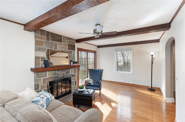 living area with baseboards, arched walkways, beam ceiling, and wood finished floors