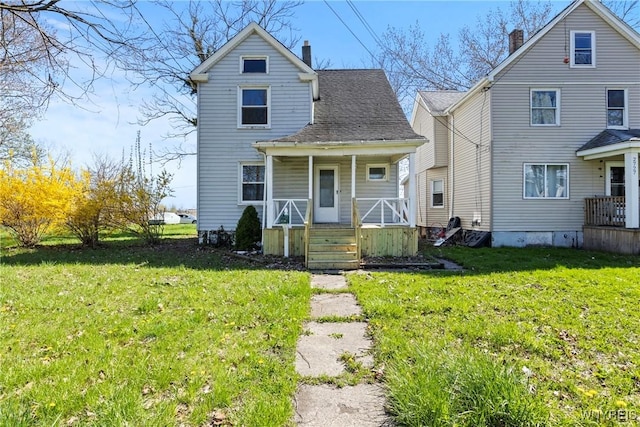 view of front of home with a porch, a shingled roof, a front lawn, and a chimney