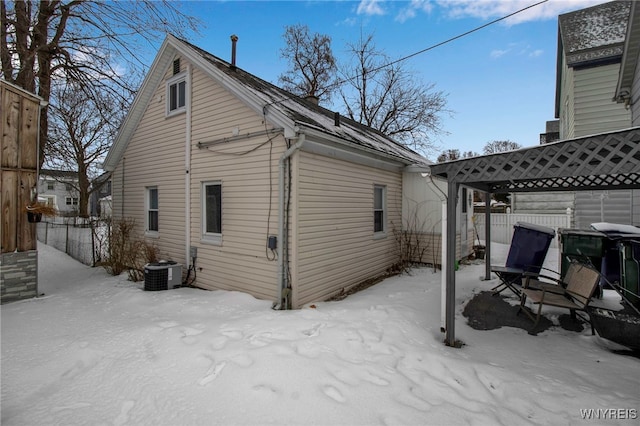snow covered back of property featuring central air condition unit and fence