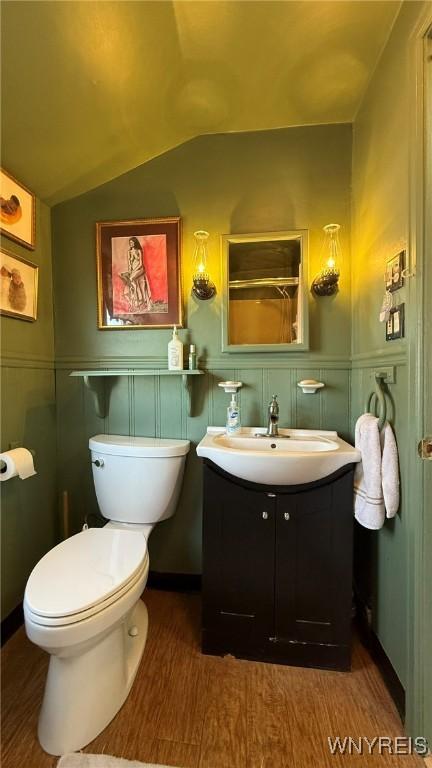 bathroom with vanity, wood finished floors, a decorative wall, toilet, and vaulted ceiling