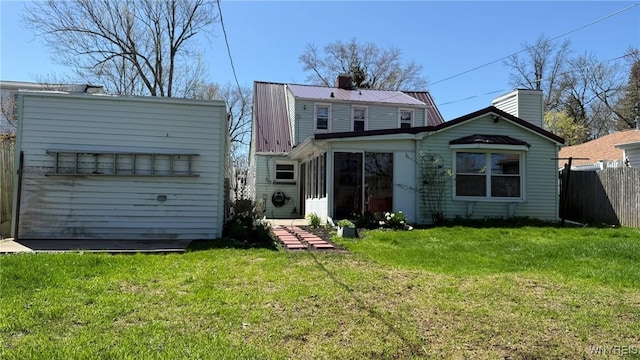 rear view of house featuring fence, a chimney, a lawn, and metal roof