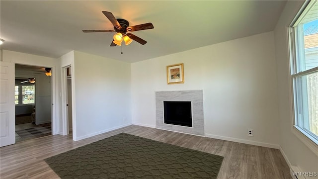 unfurnished living room featuring a tiled fireplace, baseboards, ceiling fan, and wood finished floors
