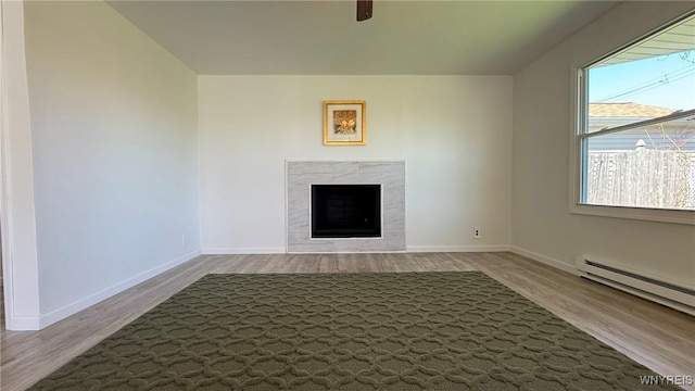 unfurnished living room with a healthy amount of sunlight, baseboards, baseboard heating, and wood finished floors