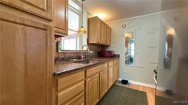 kitchen with decorative backsplash, wood finished floors, baseboards, a sink, and dark stone countertops
