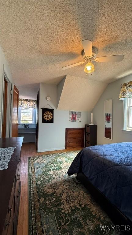 bedroom with a ceiling fan, a textured ceiling, dark wood-style flooring, and lofted ceiling