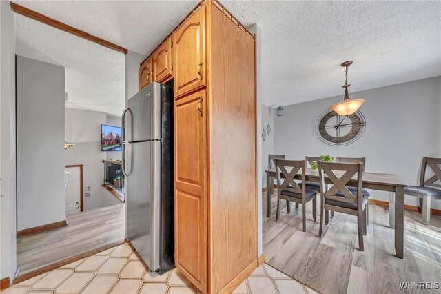 kitchen featuring a textured ceiling, hanging light fixtures, light wood-type flooring, baseboards, and freestanding refrigerator