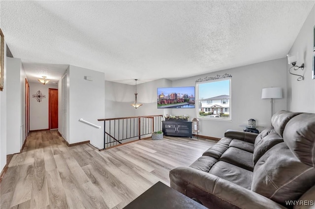 living room featuring baseboards, a textured ceiling, and light wood-style flooring