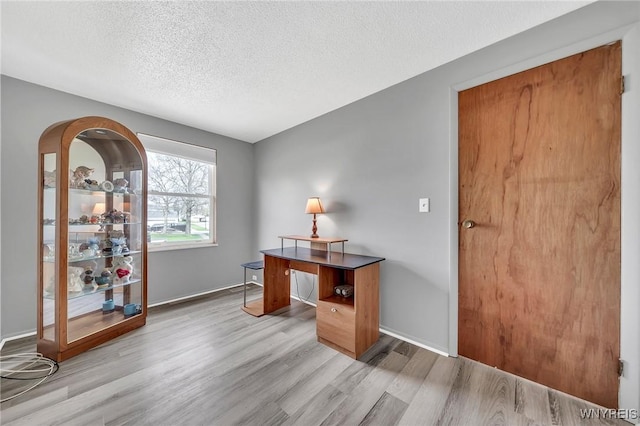 home office featuring a textured ceiling, baseboards, and light wood finished floors